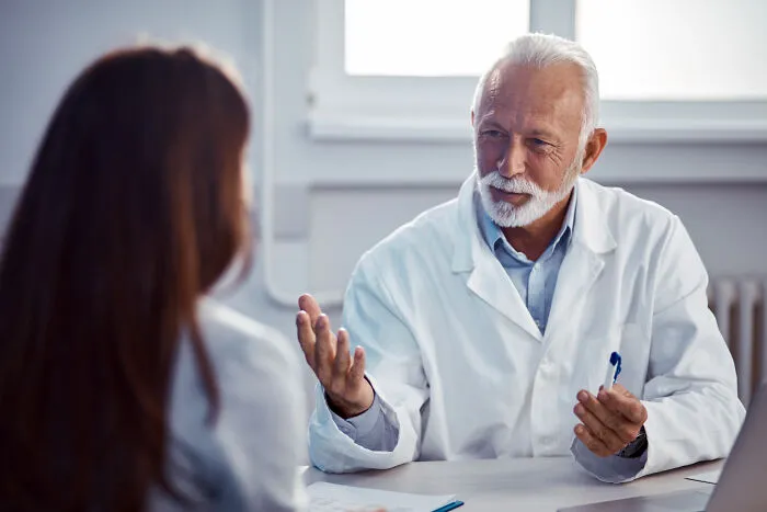 Elderly male doctor speaking dismissively to a patient in an office, illustrating bad experiences with doctors