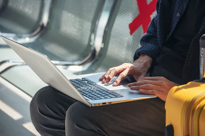 A traveler typing on a laptop at the airport terminal, representing travelers stopped by TSA