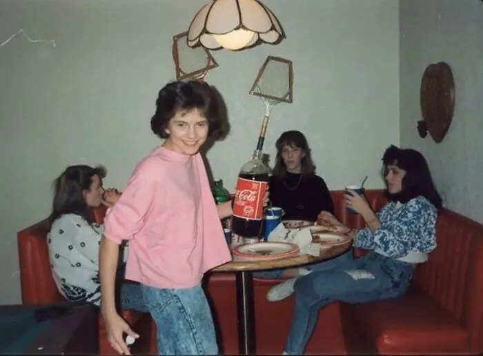 Teenagers hanging out in a booth with a 2-liter Coca-Cola bottle in one of these nostalgic photos of 80s kids.