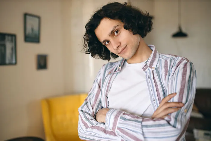 A smiling young man with curly hair posing with arms crossed, sharing experiences about living with guys.