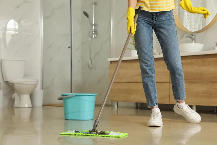 A woman mopping the bathroom floor, highlighting what it is like living with guys and managing house chores.