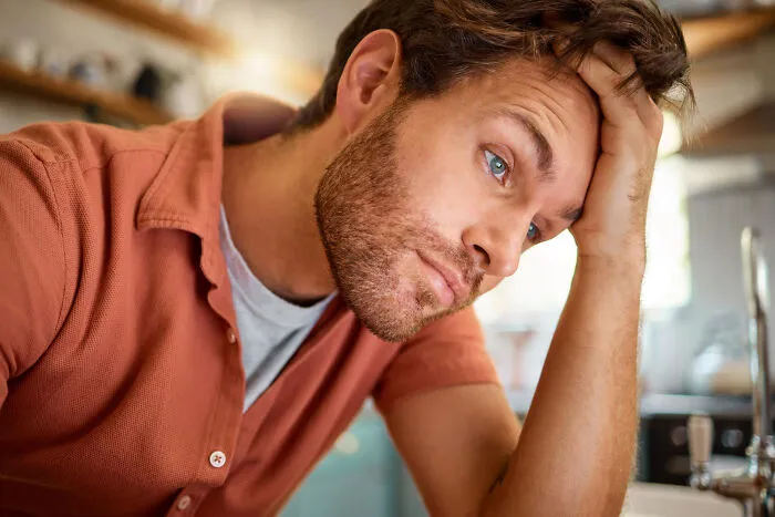 A close-up of a frustrated guy holding his hand to his head, learning about living with guys.