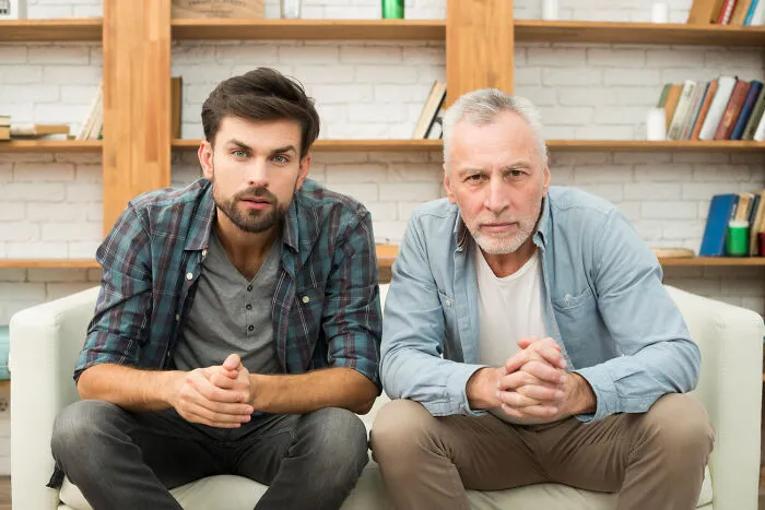 Two serious men sitting on a couch, illustrating different perspectives on living with guys