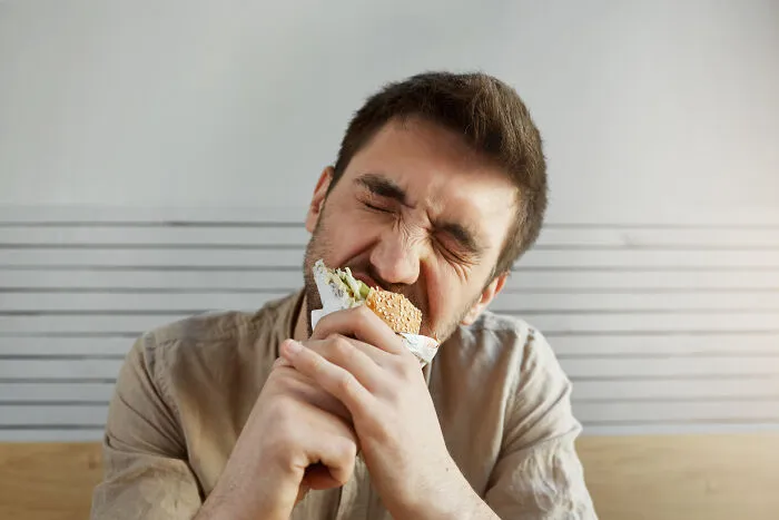 A man eagerly biting into a burger, showcasing living with guys habits