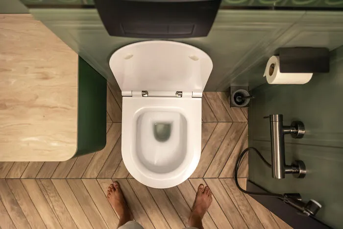 A top-down view of a modern bathroom with feet near the toilet, a reality of living with guys.