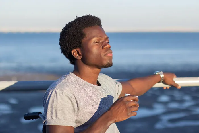 A thoughtful man in a wheelchair holds a cup outdoors, reflecting on living with guys.