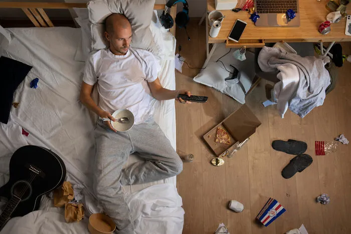 Top view of a man eating in a messy bedroom, depicting daily life living with guys