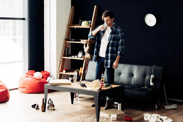Man drinking water in messy living room, highlighting the reality of living with guys
