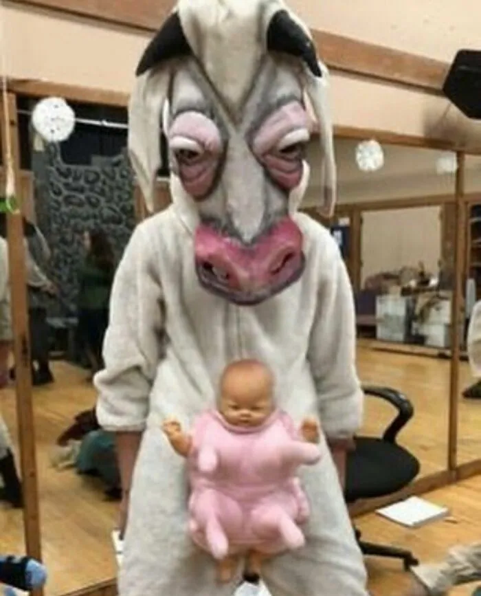Persona con disfraz de vaca y muñeco extraño colgando, imagen maldita difícil de explicar en ambiente interior.