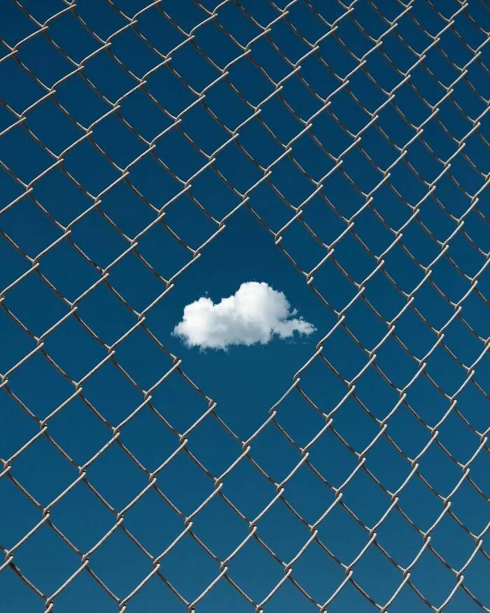 Nube blanca enmarcada en el hueco de una cerca, una creativa escena callejera urbana.