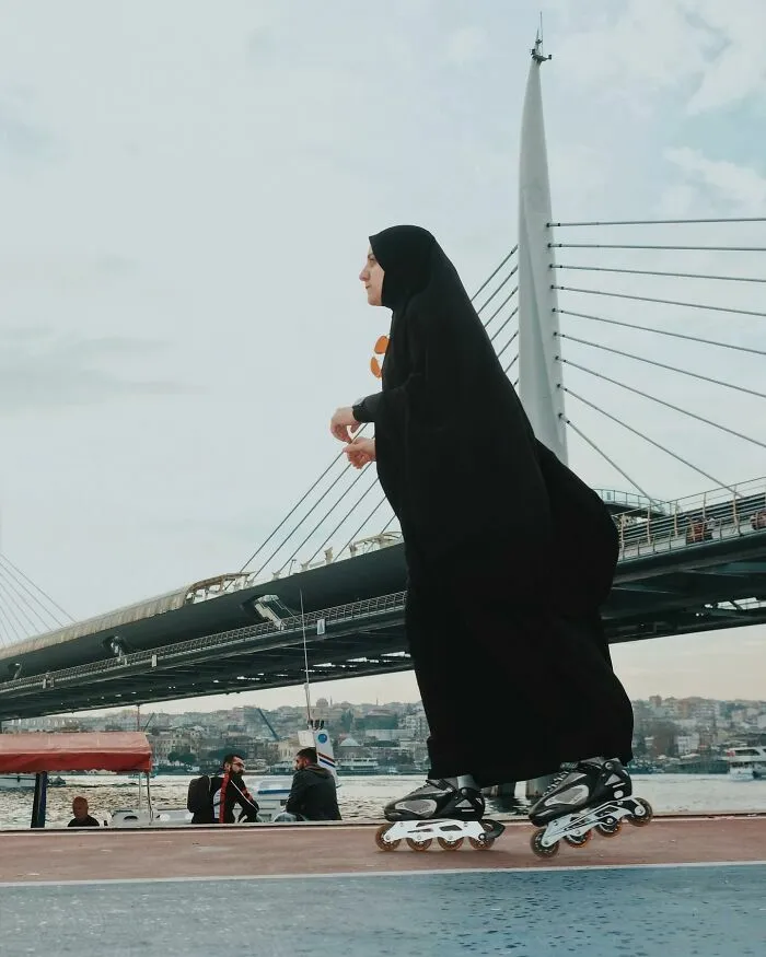 Mujer con hiyab patinando frente a un puente, captada en escenas callejeras con una sincronización perfecta.