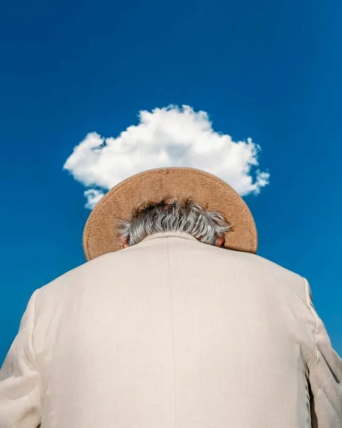 Fotografía callejera de persona con sombrero alineado perfectamente con una nube en el cielo azul.