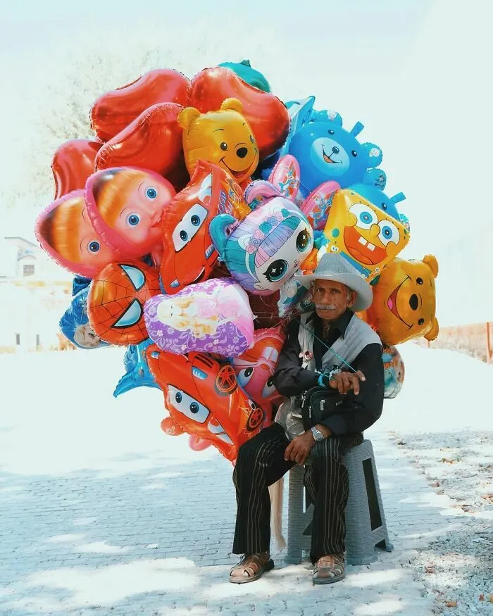 Vendedor de globos infantiles de personajes sentado en la vía pública creando escenas callejeras únicas.