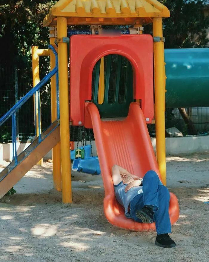 Un hombre durmiendo en un tobogán rojo captured en fascinantes escenas callejeras sincronizadas.