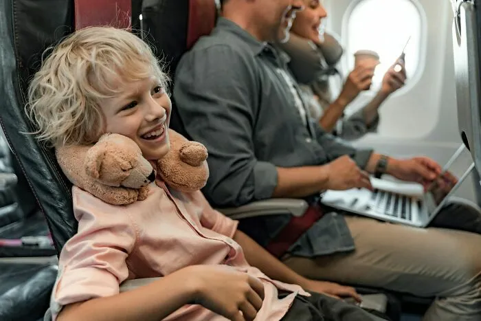 Niño sonriente sentado en avión con cuello almohada