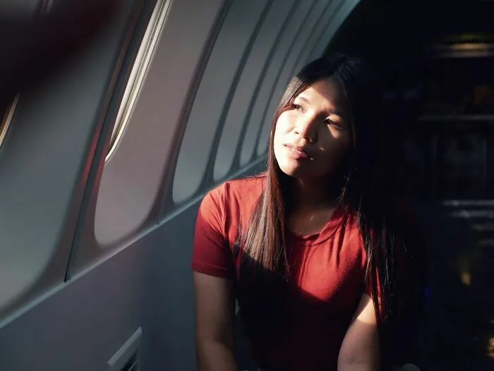 Mujer sentada junto a la ventana en avión pensando en vuelo