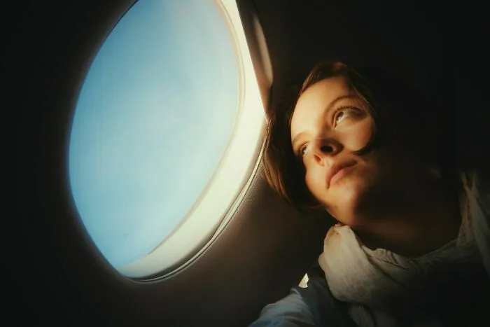 Mujer pensativa mirando por ventana de avión durante vuelo