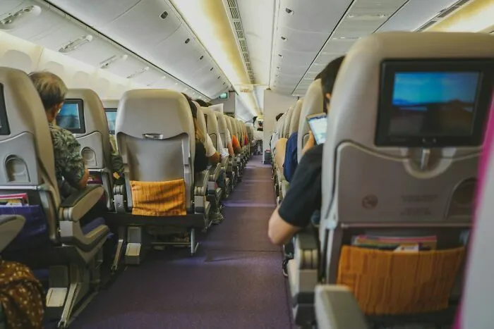 Pasajeros sentados en filas con pantallas de entretenimiento en avión