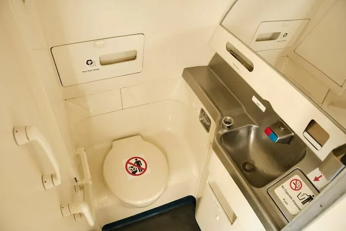 Interior del baño pequeño de avión mostrando lavabo y inodoro
