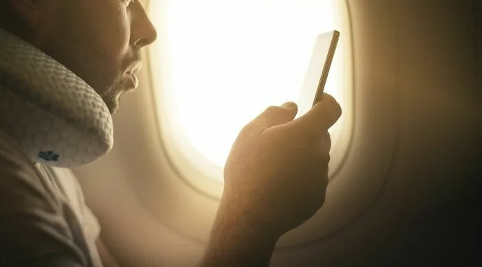 Pasajero maleducado mirando su móvil dentro de avión con almohada de viaje