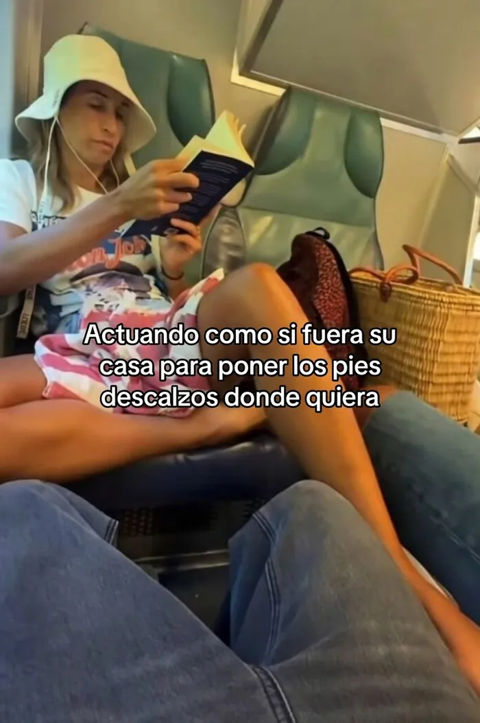 Pasajera egocéntrica con sombrero leyendo un libro y colocando sus pies descalzos sobre otro asiento.