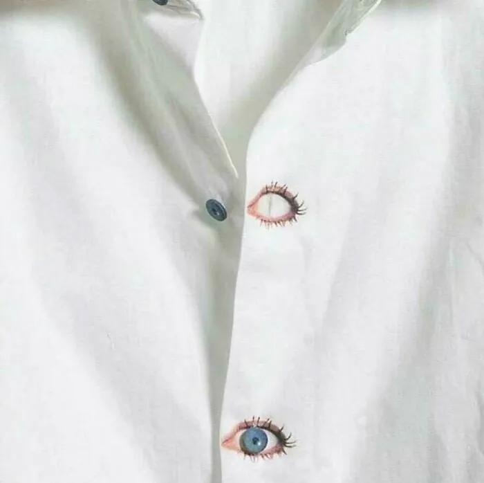 Camisa blanca con ojales bordados en forma de ojos realistas, demostrando un increible talento en costura.