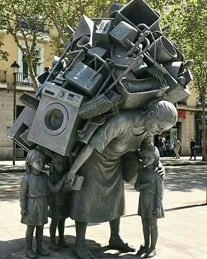 Estatua de mujer cargando utensilios de casa y ninos, cosas tan curiosas expresadas en el arte urbano.