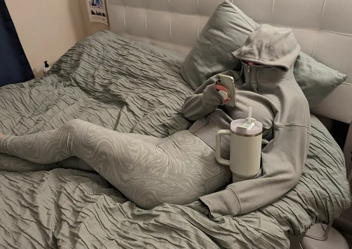 Novias y esposas con ropa cómoda en la cama usando el móvil con capucha en la cara