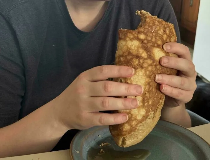 Persona comiendo un panqueque gigante doblado como taco, ilustrando errores tontos de esposas.