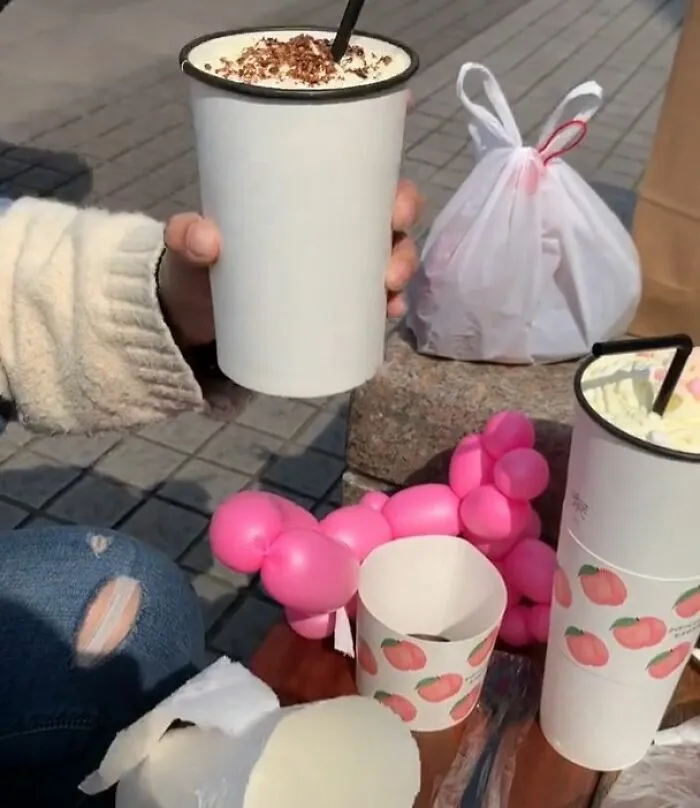 Un vaso de bebida con un soporte de globo rosa inútil hecho por diseñadores terribles.
