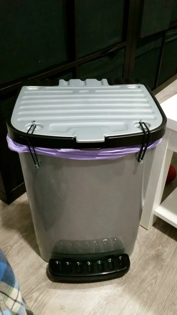 Bote de basura gris con tapa asegurada por ligas negras, parte de proyectos caseros peculiares.