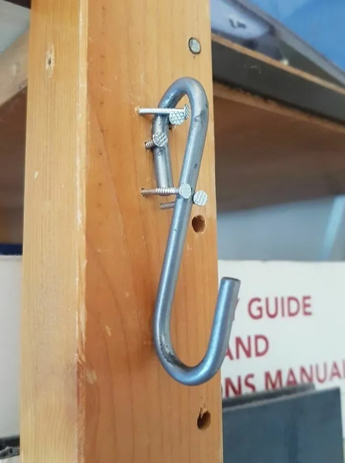 Gancho metálico sujetado de forma inestable con clavos en la madera, entre varios proyectos caseros.