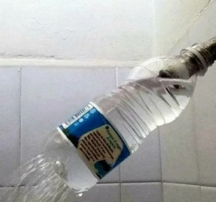 Botella de plástico usada como cabezal de ducha en proyectos caseros improvisados.