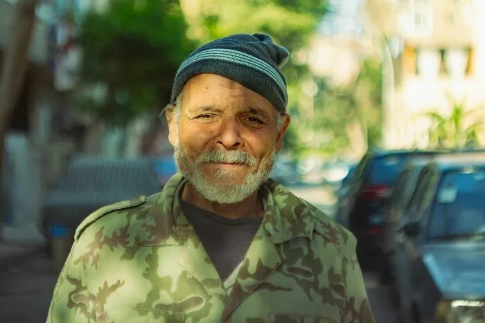 Un hombre mayor sonriente en la calle con gorro de lana, compartiendo sus historias de vida.