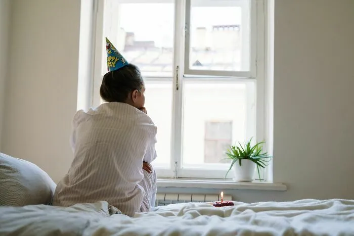 Una mujer de espaldas mirando por la ventana en su cumpleaños con un gorrito festivo