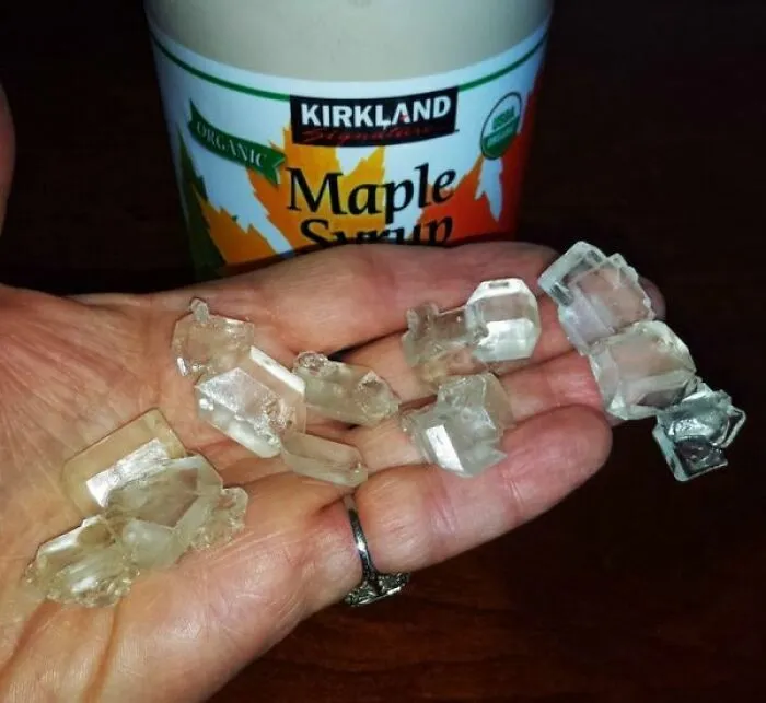 Cristales de azúcar de arce en mano con jarabe de arce de fondo