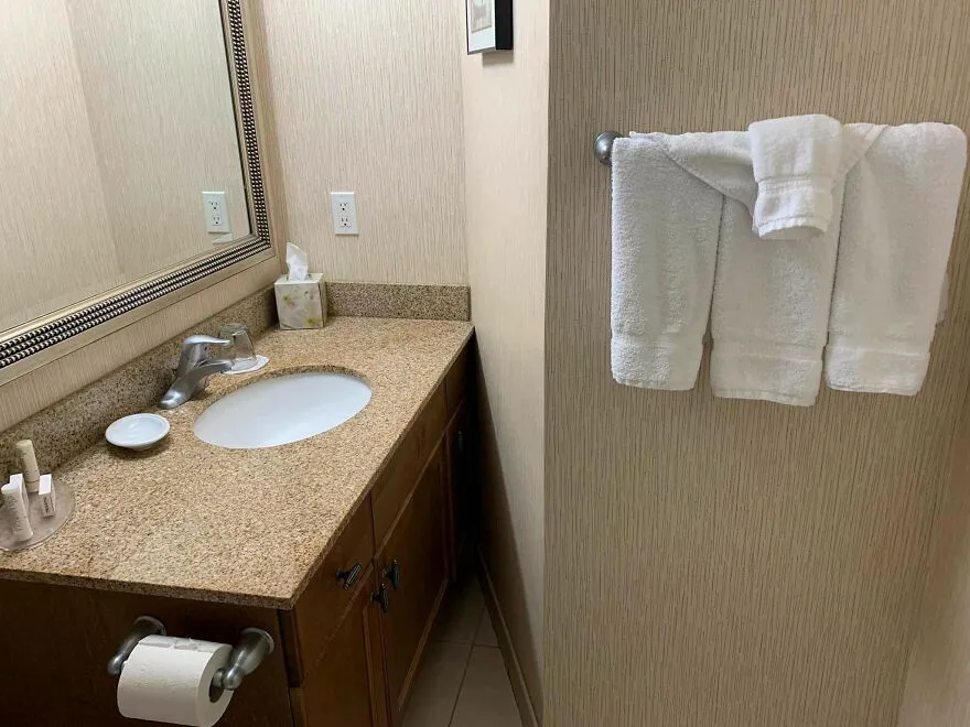 Fallo en hotel mostrando toallas dobladas como un pantalón colgadas en baño pequeño
