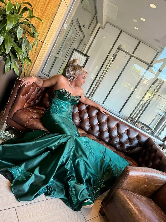 Mujer con vestido verde elegante posando en sofá marrón
