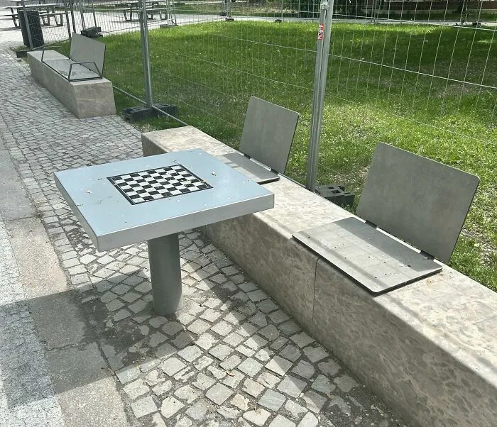 Banco con sillas metálicas incómodas y mesa con tablero de ajedrez