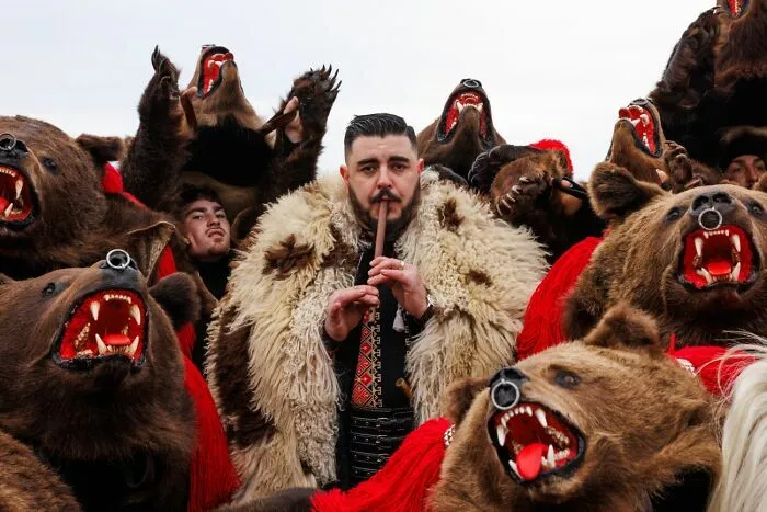 Hombre con traje tradicional rodeado de figuras con máscara de oso en los Premios internacionales de fotografía Siena
