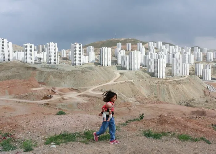Niña con muñeca camina en terreno árido frente a edificios en los Premios internacionales de fotografía Siena