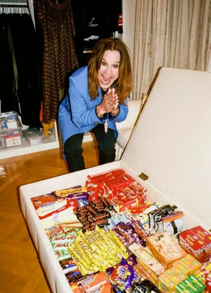 Ozzy Osbourne sonriendo emocionado junto a un baúl lleno de dulces, imágenes reconfortantes.