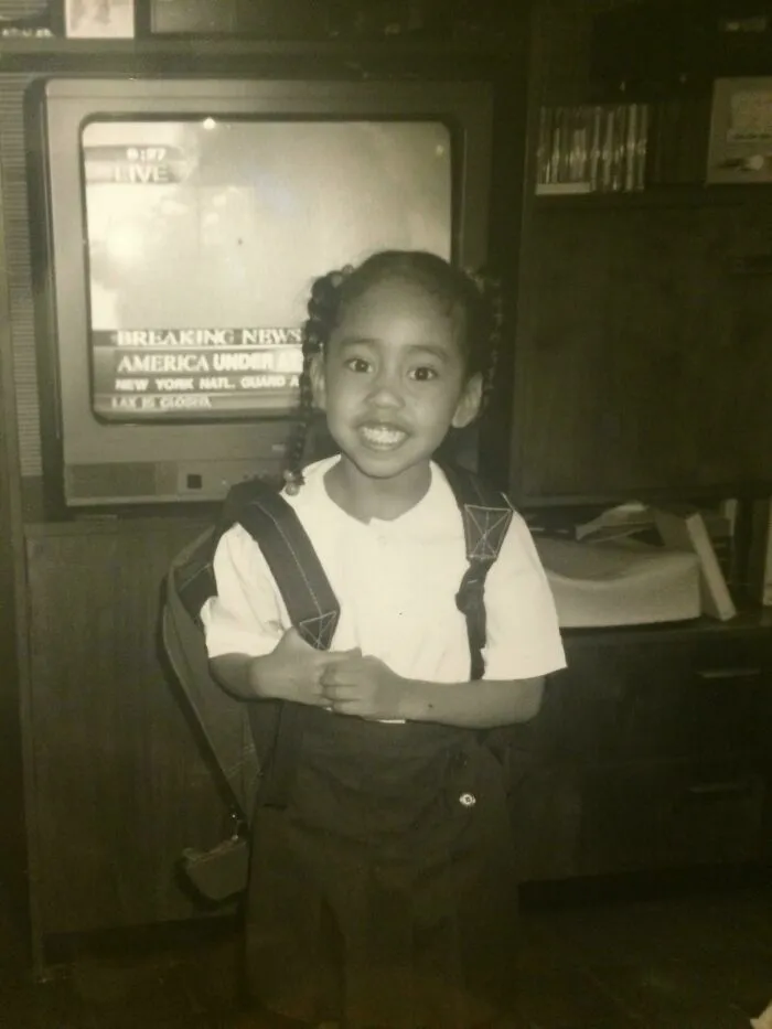 Niña posando sonriente en el colegio mientras al fondo la television transmite noticias impactantes en fotos divertidas.