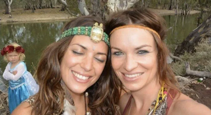 Dos mujeres sonrientes con niña molesta en el fondo mostrando un fondo cómico