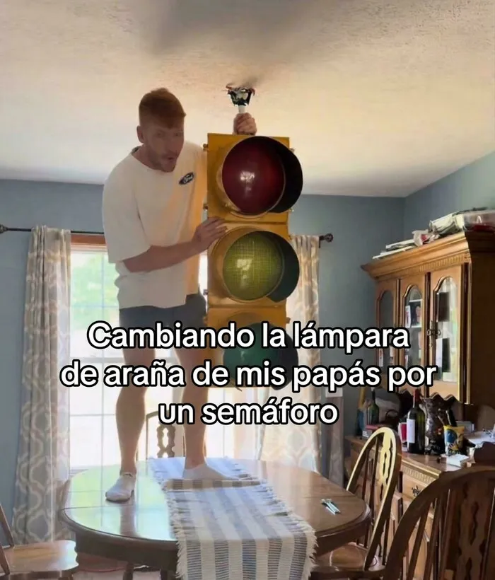 Hombre parado sobre una mesa cambiando una lámpara por un semáforo, mostrando ignorancia en TikTok.