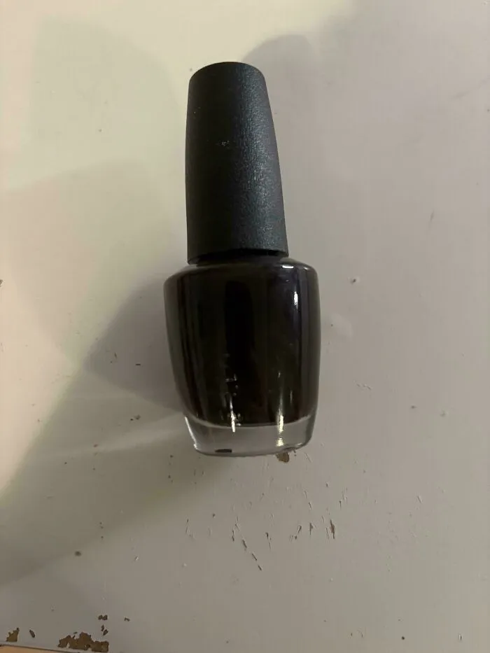 Frasco de esmalte de uñas oscuro sobre una superficie, mostrando fallos de diseño