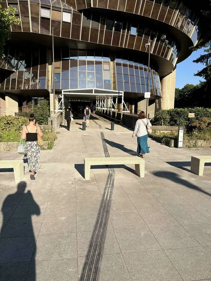 Guía táctil para ciegos bloqueada por un banco de concreto, fallo de diseño de accesibilidad.