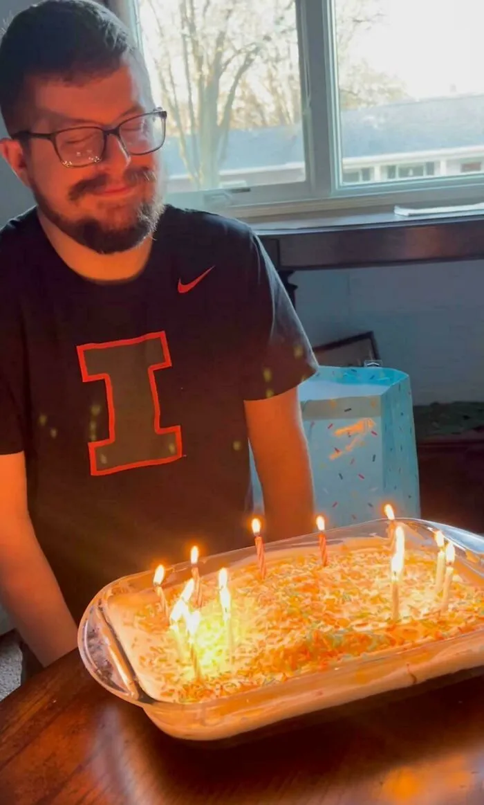 Hombre sonriendo frente a pastel con velas encendidas, publicaciones reconfortantes.