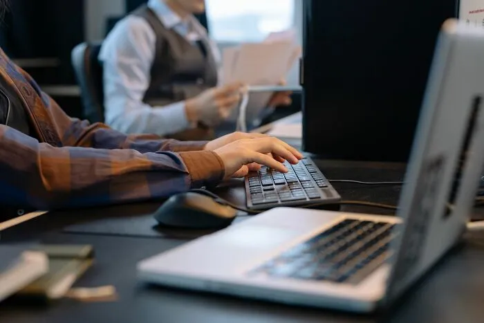Manos de trabajadores escribiendo en un teclado dentro de una oficina.