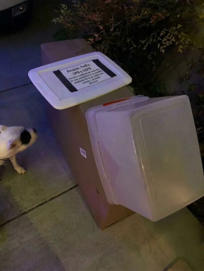 Acción curiosa de repartidores al cubrir una gran caja con un pequeño contenedor de plástico.